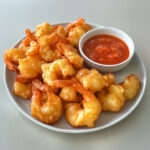 Beignets dorés de crevettes croustillantes, servis avec sauce soja et coriandre fraîche sur une assiette colorée.