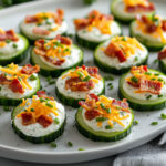 Bouchées apéritives de concombre garnies de crème, cheddar et lardons croustillants, servies bien fraîches avec herbes en décoration.