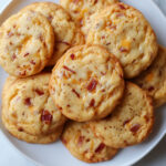 Cookies salés dorés au cheddar, cumin et lardons, croustillants à l’extérieur et fondants à l’intérieur, sur une grille de refroidissement.