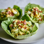 Coupelles de laitue garnies de crème d’avocat, œufs durs et lardons croustillants, servies fraîches pour une entrée gourmande et estivale.