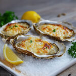 Huîtres gratinées dorées au four sur lit de gros sel, garnies de crème à l’échalote, fromage et persil frais.