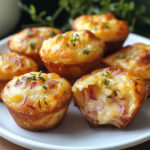 Mini muffins dorés au fromage et oignons rouges, servis tièdes en bouchées moelleuses et savoureuses.