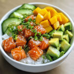 Bol de poke bowl coloré avec saumon cru mariné, avocat, concombre et mangue sur lit de riz à sushi.