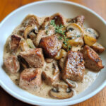 Plat de sauté de porc crémeux aux champignons de Paris servi avec du riz, décoré de thym frais.